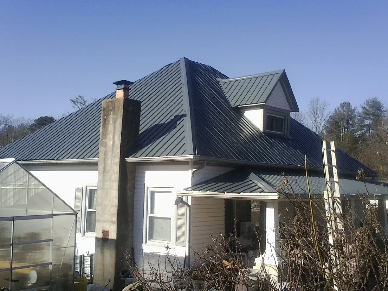 Dark blue standing seam metal roof on a white farmhouse with dormer — Slate & Tile Roof Repair by Roofing Brothers in North Augusta