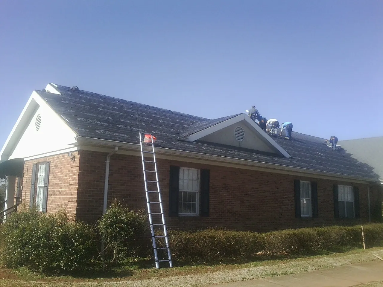 Crew tearing shingles off a brick ranch roof with a ladder set — Emergency Roof Repair work by our crew in North Augusta