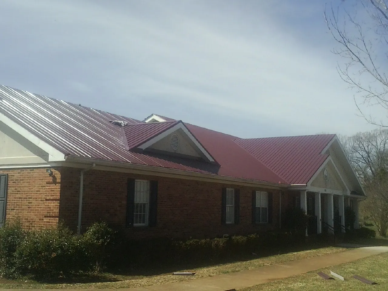 Red metal roof with gabled entries on a long brick building, from a Hail Damage Roof Repair job in North Augusta
