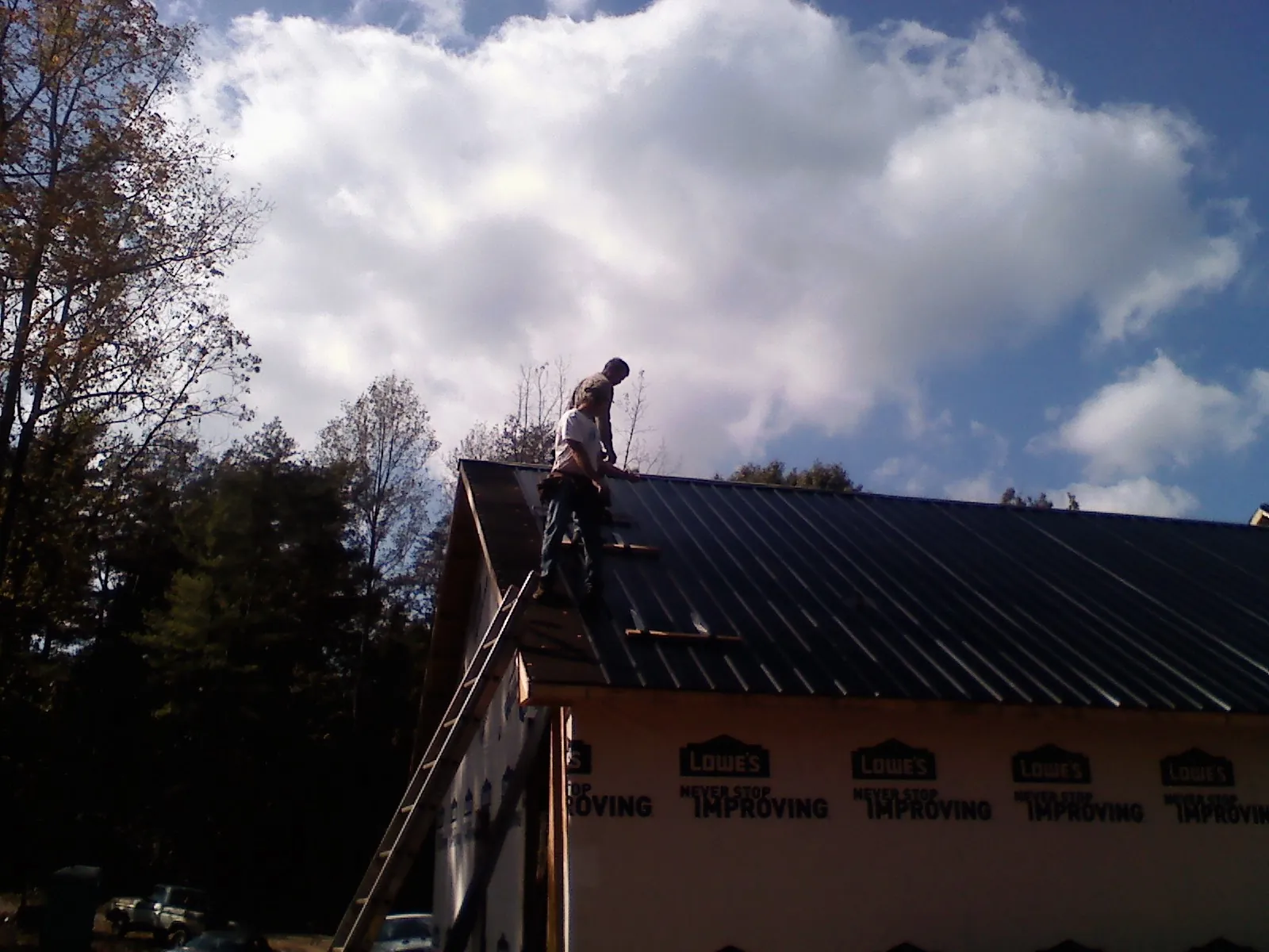 Roofer fastening dark metal panels high against a cloudy sky, from a Roof Inspection job in North Augusta