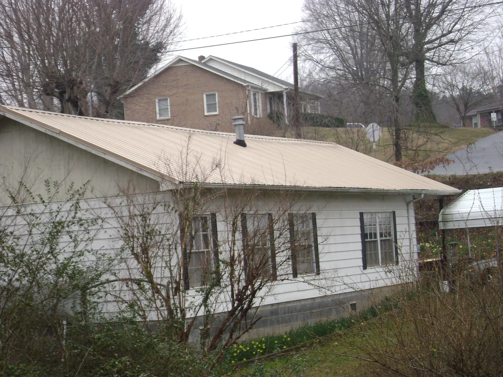 Tan metal roof on a white sided house set into a hillside — Commercial Roofing by Roofing Brothers in North Augusta